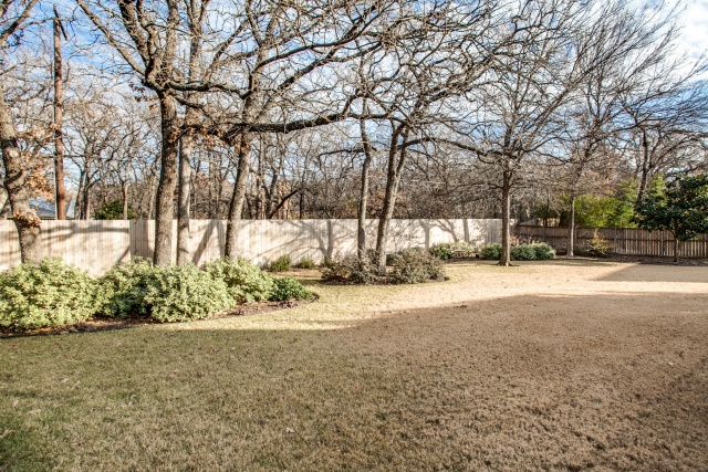 The huge treed backyard is surrounded by a wood fence.